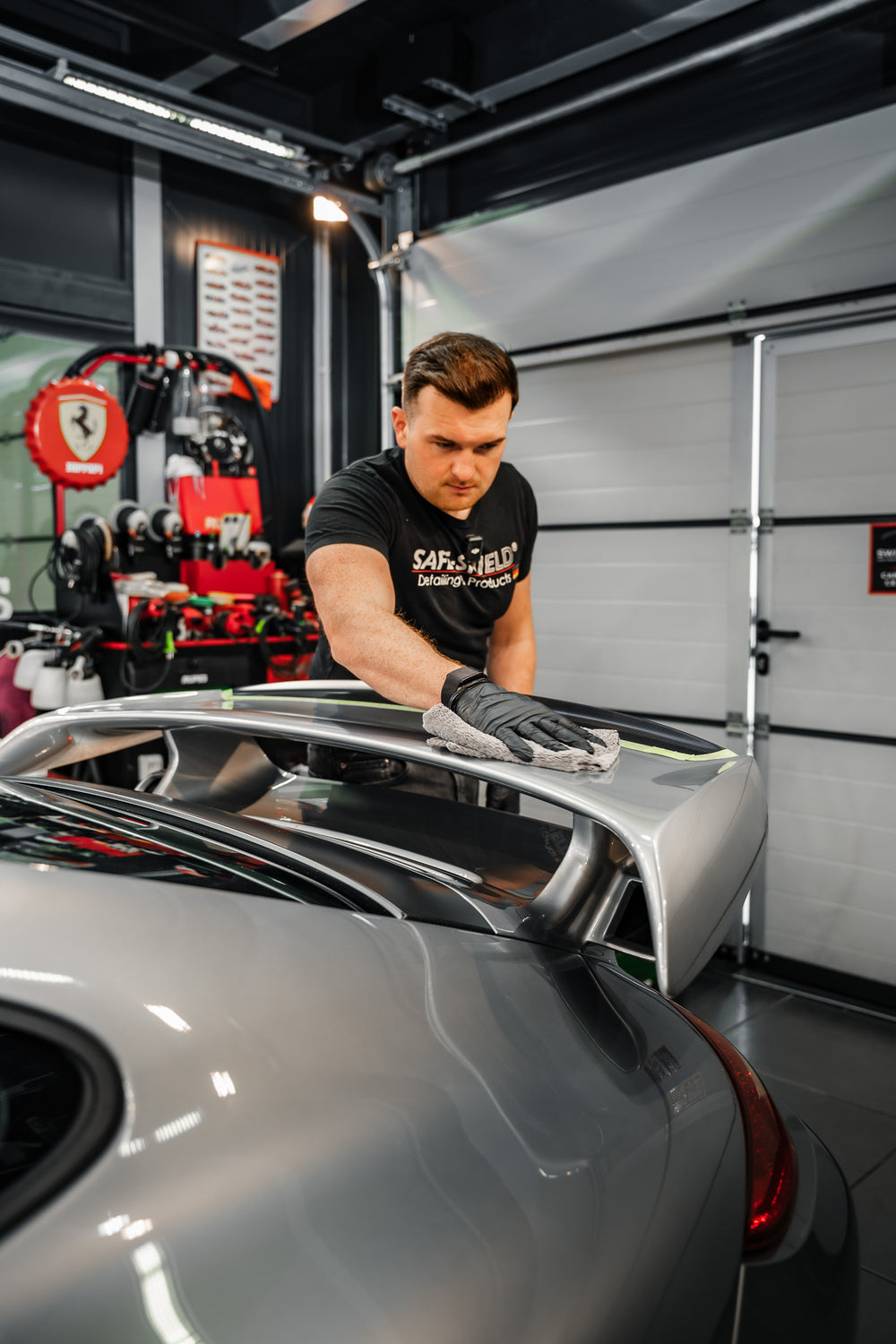 Tim retire des résidus du spoiler arrière d’une voiture de sport avec la microfibre grise de 400 GSM