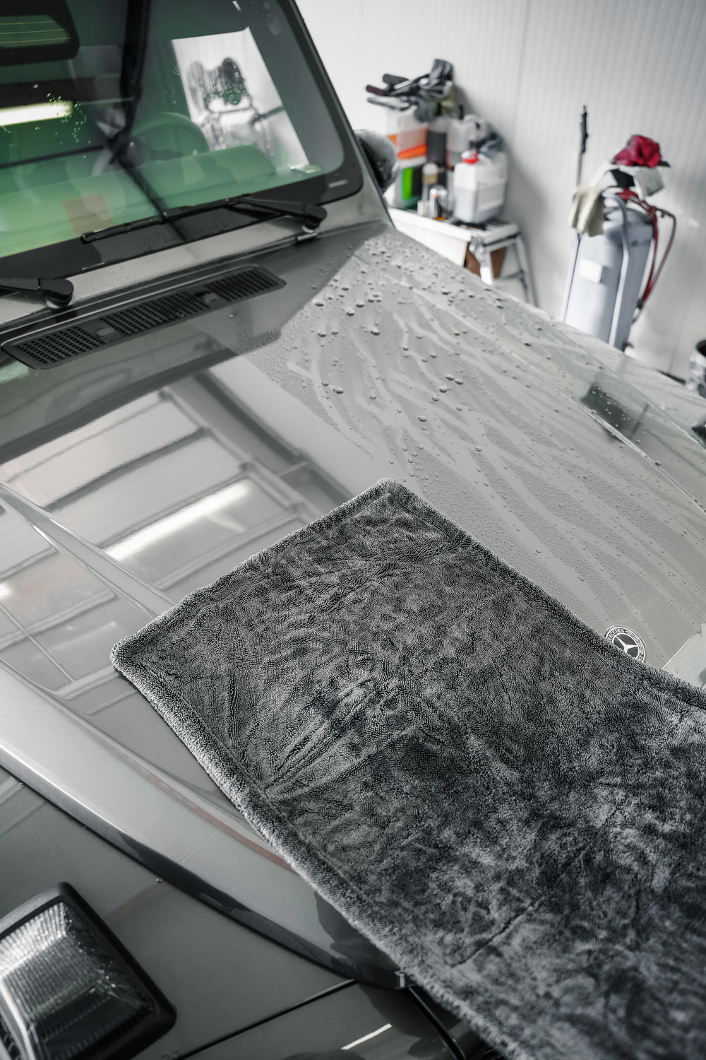 Microfibre de séchage grise de 1600 GSM sur un capot, avec une zone déjà sèche et des gouttes d’eau restantes