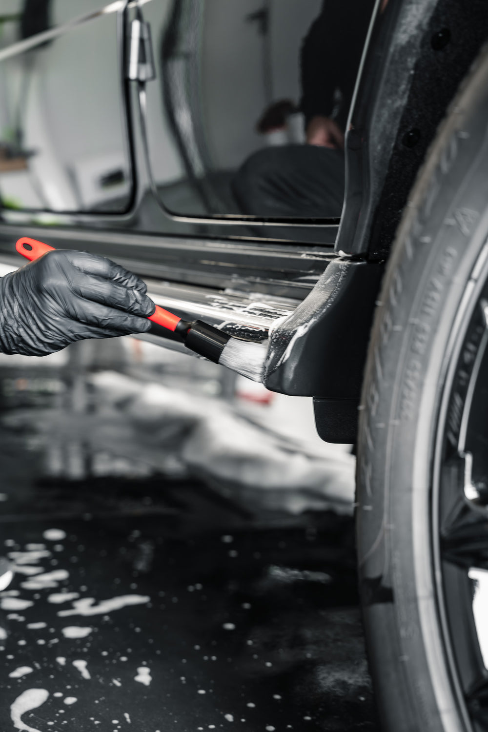 Pinceau de detailing Allround gris nettoyant une zone recouverte de mousse sur le bas de caisse d’un véhicule